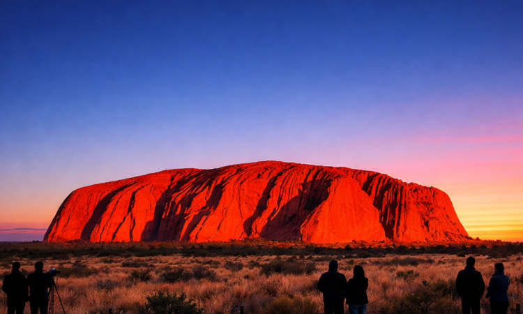 Uluru glowing orange at sunrise with visitors watching from viewing area in Red Centre