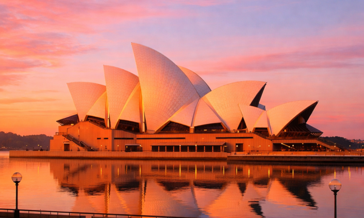 Sydney Opera House at sunrise with golden light on white sails and harbour reflections